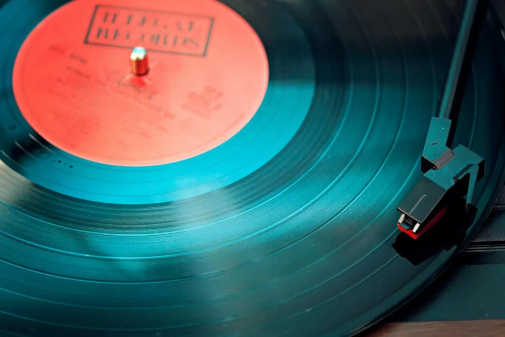 Disco de vinilo de color negro con etiqueta roja en el centro, fabricado en Policloruro de Vinilo (PVC), material duradero que se utiliza comúnmente en discos de música y otros productos debido a su resistencia a los agentes atmosféricos.